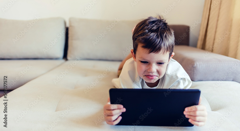 Happy little boy watching cartoons on digital tablet. Cute happy boy enjoying while using touchpad at homea. Copy space. Happy little boy watching cartoons on digital tablet. Cute happy boy enjoying while using touchpad at homea. Copy space.
