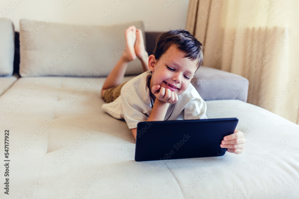 Happy little boy watching cartoons on digital tablet. Cute happy boy enjoying while using touchpad at homea. Copy space. Happy little boy watching cartoons on digital tablet. Cute happy boy enjoying while using touchpad at homea. Copy space.