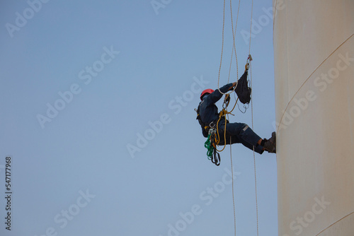 Top view pic of industrial rope access welder working at height wearing harness, helmet safety equipment rope access inspection of thickness storage tank