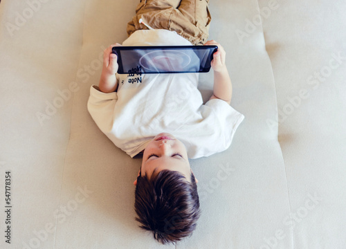 Happy little boy watching cartoons on digital tablet. Cute happy boy enjoying while using touchpad at homea. Copy space. photo