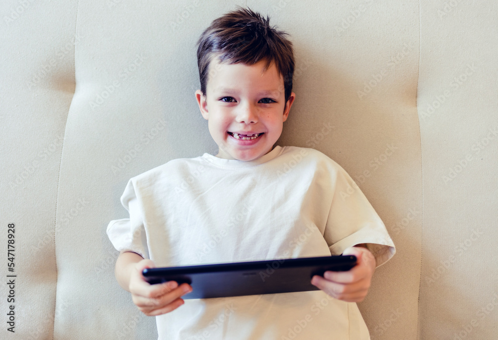 Little boy using digital tablet. Little boy with digital tablet sitting on sofa, on home interior background. Little boy reading an ebook. Growing up in a technology-based world. Little boy using digital tablet. Little boy with digital tablet sitting on sofa, on home interior background. Little boy reading an ebook. Growing up in a technology-based world.