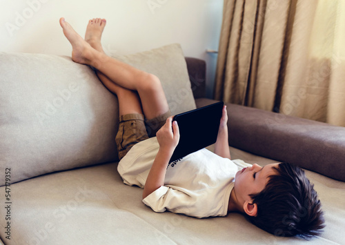Boy playing with digital tablet. Cute little boy playing with a tablet pc on sofa at home.