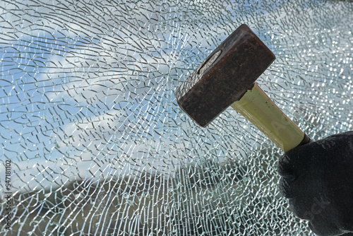 Gloved hands of a criminal destroying a laminated glass window with a hammer, violence, burglary and vandalism concept, copy space
