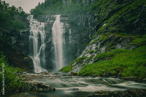 Long exposure shot of a Skjervefossen waterfall in a valley emerging from the forest in Bergen area photo