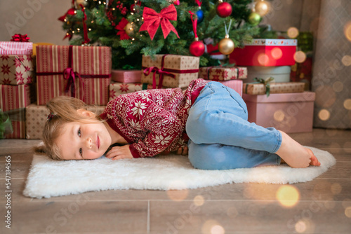 Child girl lies near the Christmas tree and dreaming. Merry Christmas! Adorable child girl dreaming near a Christmas tree