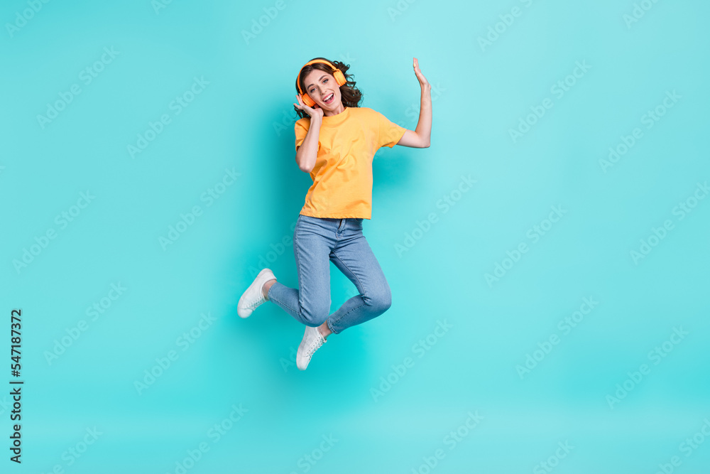 Full length photo of shiny pretty lady wear yellow t-shirt jumping high enjoying music isolated turquoise color background