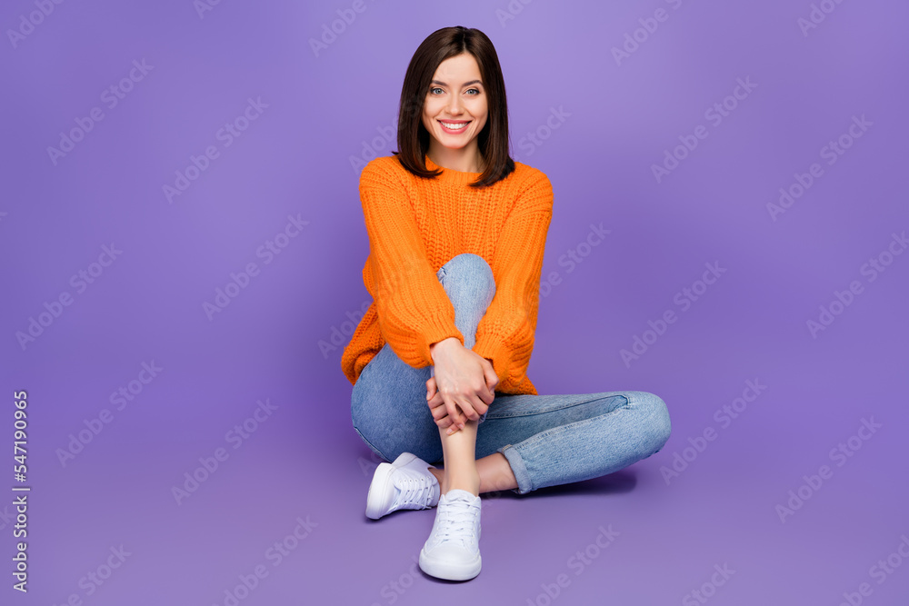 Full body photo of pretty young woman sitting floor hug knee smiling wear trendy knitwear orange outfit isolated on violet color background Full body photo of pretty young woman sitting floor hug knee smiling wear trendy knitwear orange outfit isolated on violet color background
