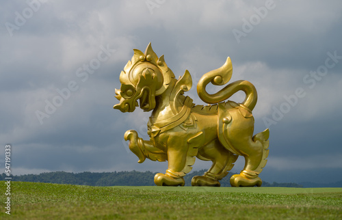 Singha statue. A big golden lion statue standing at green grass at Singha park. Chiang Rai, Thailand © daphnusia