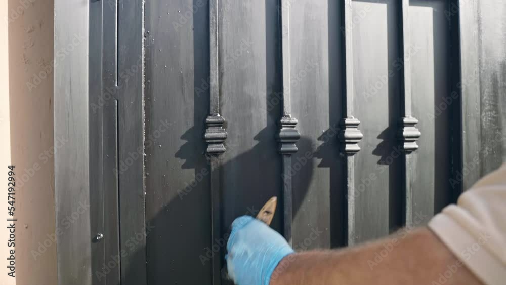 Repairman colouring steel gate with black paint on construction site, restoration process of an old corroded gate with chemical solutions and special repairing equipment and tools. Workman in Repairman colouring steel gate with black paint on construction site, restoration process of an old corroded gate with chemical solutions and special repairing equipment and tools. Workman in