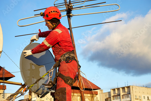 A specialist repairs an antenna on the roof. Rope access