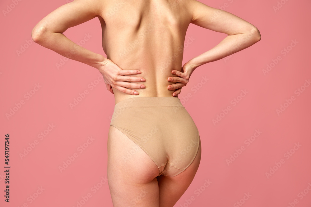 Cropped back view image of female body, back buttocks in beige underwear isolated over pink studio background