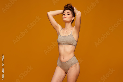 Portrait of young beautiful woman posing in grey underwear isolated over yellow studio background. Sensuality and femininity
