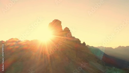 Sun rises over mountain range. High rocky peaks with sand-covered foothills of Three Peaks of Lavaredo under cloudless sky aerial view in back lit photo