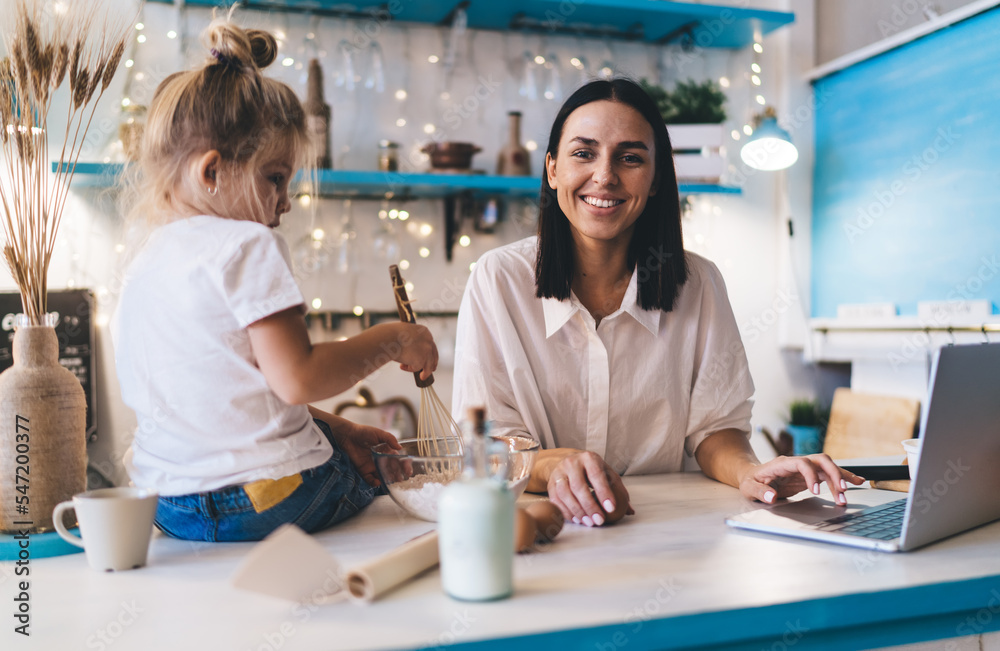 Smiling mother in kitchen with laptop and daughter