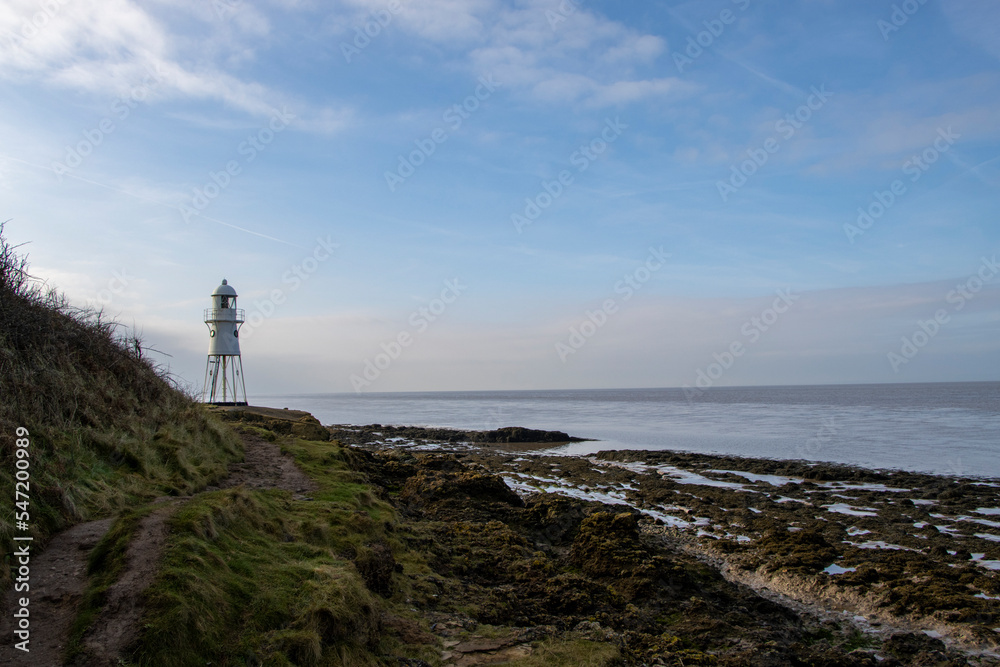 Lighthouse tower by the sea with coast and clouds