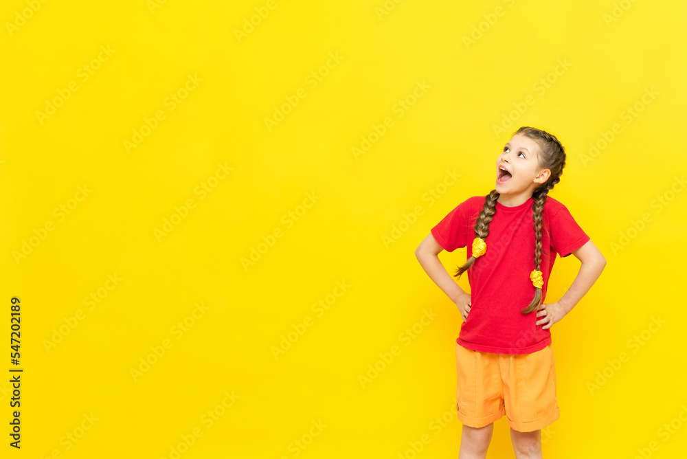 A little girl looks at the space for your advertisement, isolated yellow. A schoolgirl in a red T-shirt is looking at your ad in an empty space. A little girl looks at the space for your advertisement, isolated yellow. A schoolgirl in a red T-shirt is looking at your ad in an empty space.