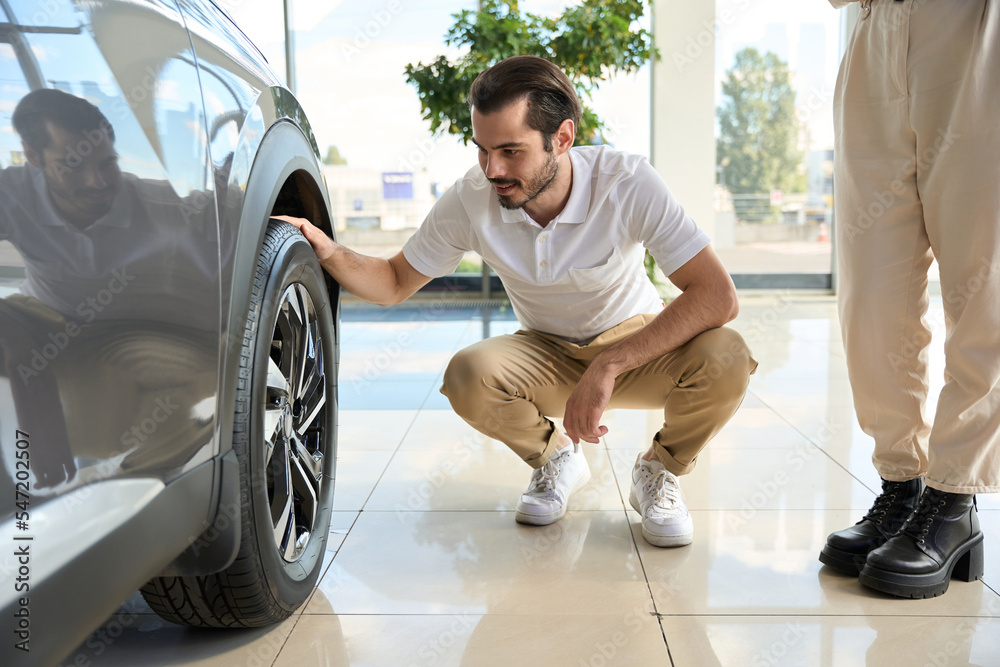 Smiling automotive buyer checking auto tire condition in showroom Smiling automotive buyer checking auto tire condition in showroom