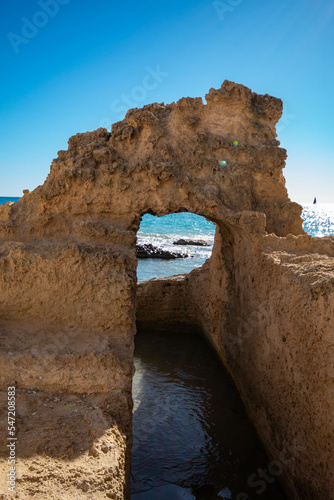 Arco de piedra por donde pasa el agua del rio hacia el mar mediterráneo de la playa de Calpe en Alicante bajo un precioso cielo azul.