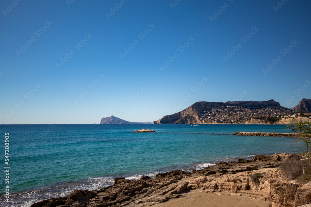 Gran panorámica del pequeño pueblo de Calpe con el tranquilo mar Mediterráneo bajo un precioso cielo azul soleado. Gran panorámica del pequeño pueblo de Calpe con el tranquilo mar Mediterráneo bajo un precioso cielo azul soleado.