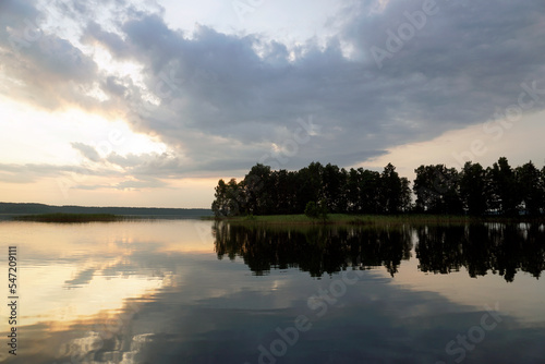 Fototapeta Naklejka Na Ścianę i Meble -  Evening on the lake in summer in July. The sun and sky are reflected on the calm surface of the water. Soft light and bright colors. Sunset and pacification	