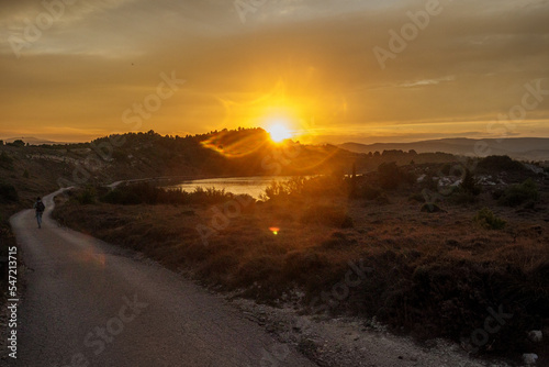 Sunset over a pond with hiker and his dog on the path, promeneuse et son chien au soleil couchant sur l'étang de Peyriac