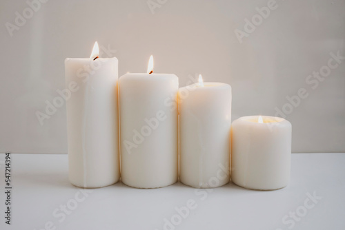 Large burning candles on the background of a white wall.