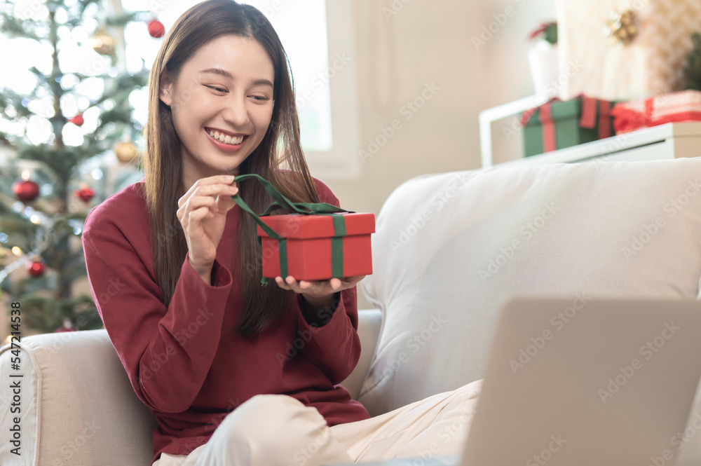 Young beautiful Asian woman use notebook computer connect video call talking, greeting with friend, family when opening received Christmas gift box present at home. Christmas holiday festival concept. Young beautiful Asian woman use notebook computer connect video call talking, greeting with friend, family when opening received Christmas gift box present at home. Christmas holiday festival concept.