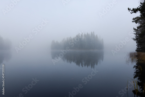 Foggy and cold late autumn morning by the lake in Finland. Island surounded by the fog.