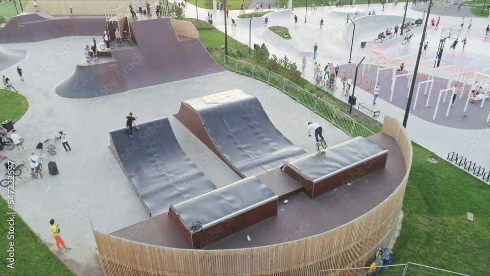 Sportsmen with bike and kick scooter ride along ramps on sports ground upper view. Public place for extreme training in park
