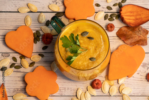 Bowl of pumpkin soup, pieces of pumpkin and seeds on wooden background. Top view 