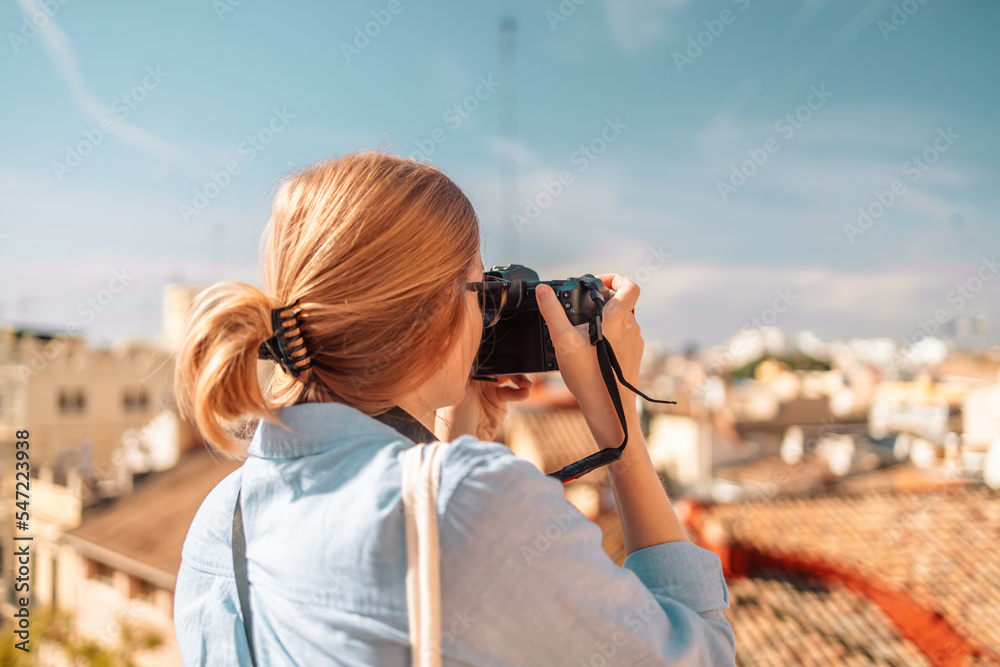Positive woman tourists photographing taking picture of house with camera at sunset at old city of Valencia, Spain. Back view Positive woman tourists photographing taking picture of house with camera at sunset at old city of Valencia, Spain. Back view