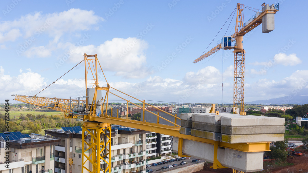 Aerial view of a industrial tower crane operating in high building construction site. These large machines allow the concrete plates weight balance. City development concept.