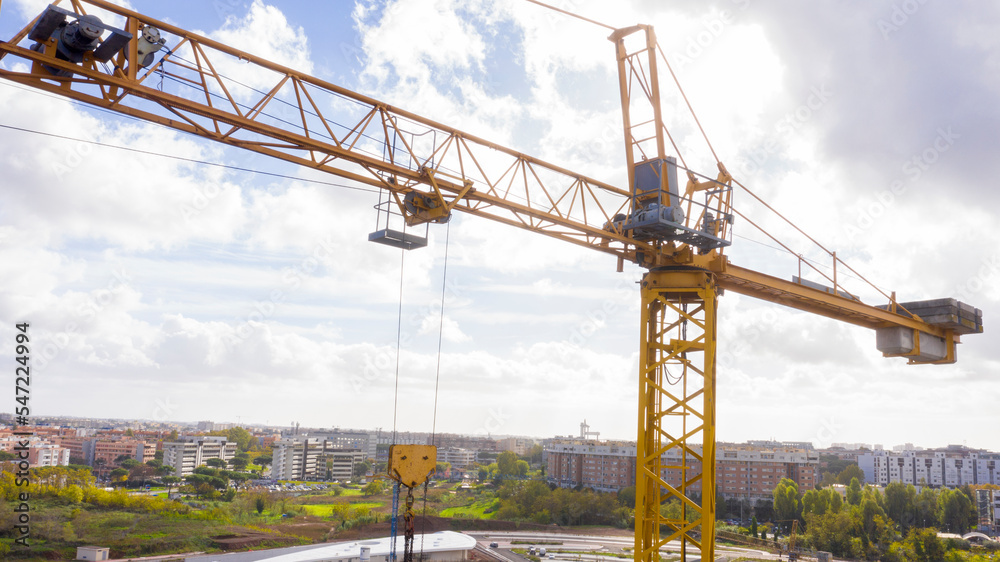 Aerial view of a industrial tower crane operating in high building construction site. These large machines allow the concrete plates weight balance. City development concept.