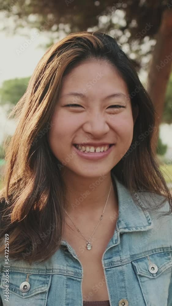 VERTICAL VIDEO: Laughing young woman posing at camera while standing in park VERTICAL VIDEO: Laughing young woman posing at camera while standing in park