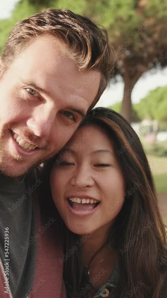 VERTICAL VIDEO: Close up, laughing couple hugging each other while standing in the park VERTICAL VIDEO: Close up, laughing couple hugging each other while standing in the park