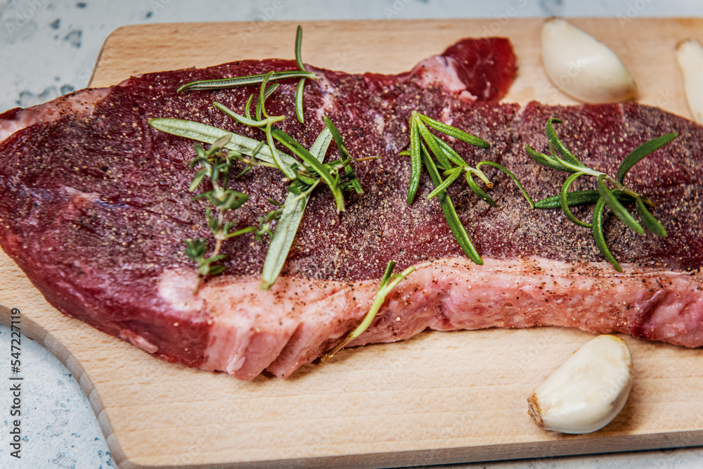 Seasoned raw sirloin beef steak on cutting board with thyme rosemary and garlic