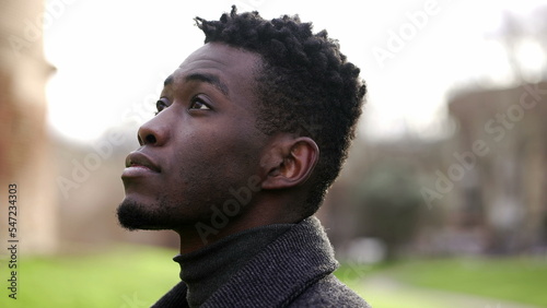 Handsome elegant black African man standing outside at park looking up at sky