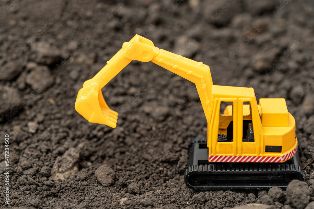 Toy model of a yellow excavator on the background of the earth with silver coins. Lean or cost building concept Toy model of a yellow excavator on the background of the earth with silver coins. Lean or cost building concept