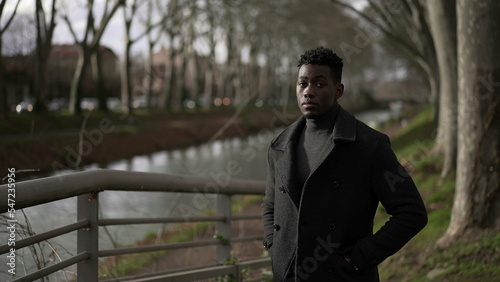 Elegant young black man standing outside at park wearing winter clothing coat