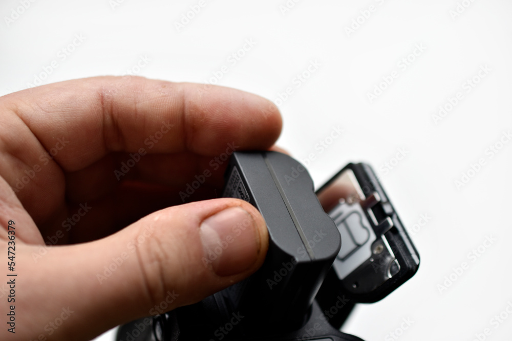 The battery of the SLR camera. Changing the camera battery in close-up. The camera battery is in the photographer's hand. The battery of the SLR camera. Changing the camera battery in close-up. The camera battery is in the photographer's hand.