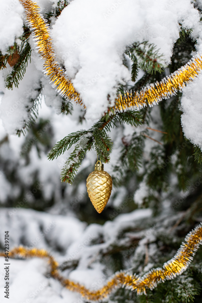 Christmas decoration on the tree under the snow. Christmas toy on the tree. Golden cone Christmas decoration on the tree under the snow. Christmas toy on the tree. Golden cone