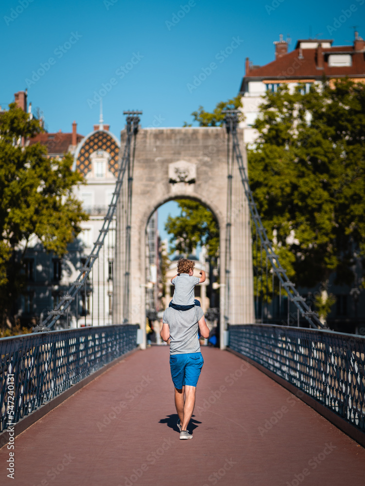 Father holding his child on his shoulders on a bridge of the city of Lyon (France), during a sunny summer day.