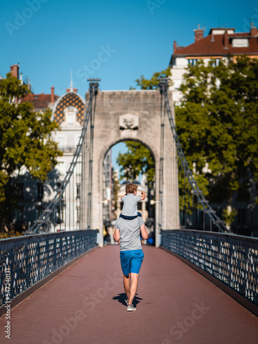 Father holding his child on his shoulders on a bridge of the city of Lyon (France), during a sunny summer day.
