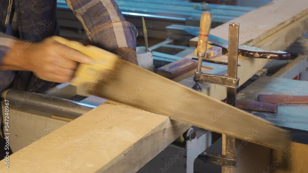 The carpenter cuts wood in the workshop.
Close-up carpenter is cutting wood with a handsaw.
