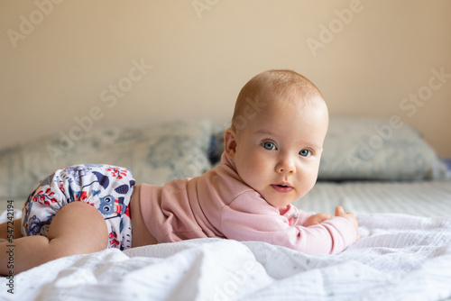 A happy, content baby lying on her stomach doing tummy time to strengthen her back. She is wearing a modern, reusable cloth diaper photo