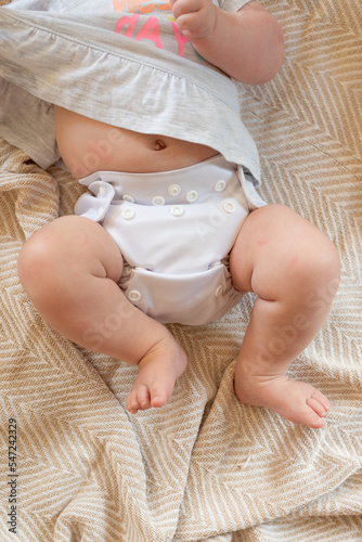 A baby lying on a bed with the focus on the baby's legs. She is wearing a modern, reusable cloth diaper with a pretty print.