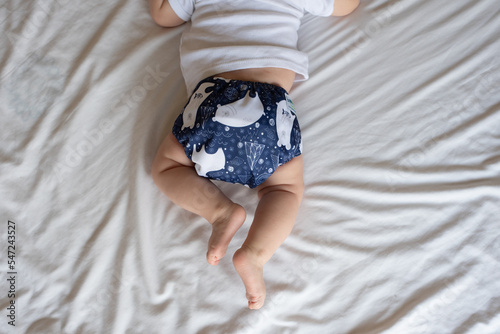 A happy, content baby lying on her stomach doing tummy time to strengthen her back. She is wearing a modern, reusable cloth diaper photo