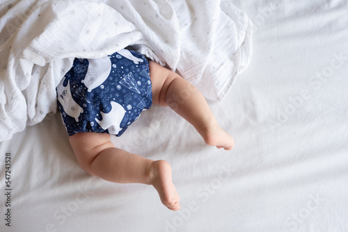 A happy, content baby lying on her stomach doing tummy time to strengthen her back. She is wearing a modern, reusable cloth diaper