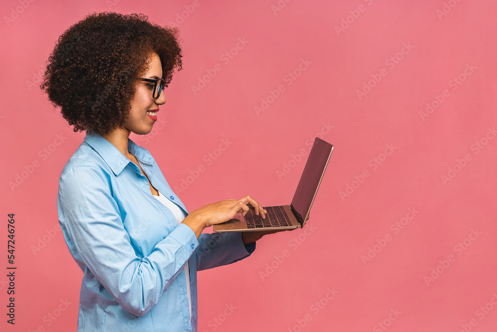Young african american black positive cool lady with curly hair using laptop and smiling isolated over pink background. Young african american black positive cool lady with curly hair using laptop and smiling isolated over pink background.