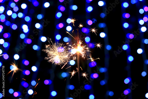 Burning sparklers at night against the background of glowing lights of a garland. Merry Christmas